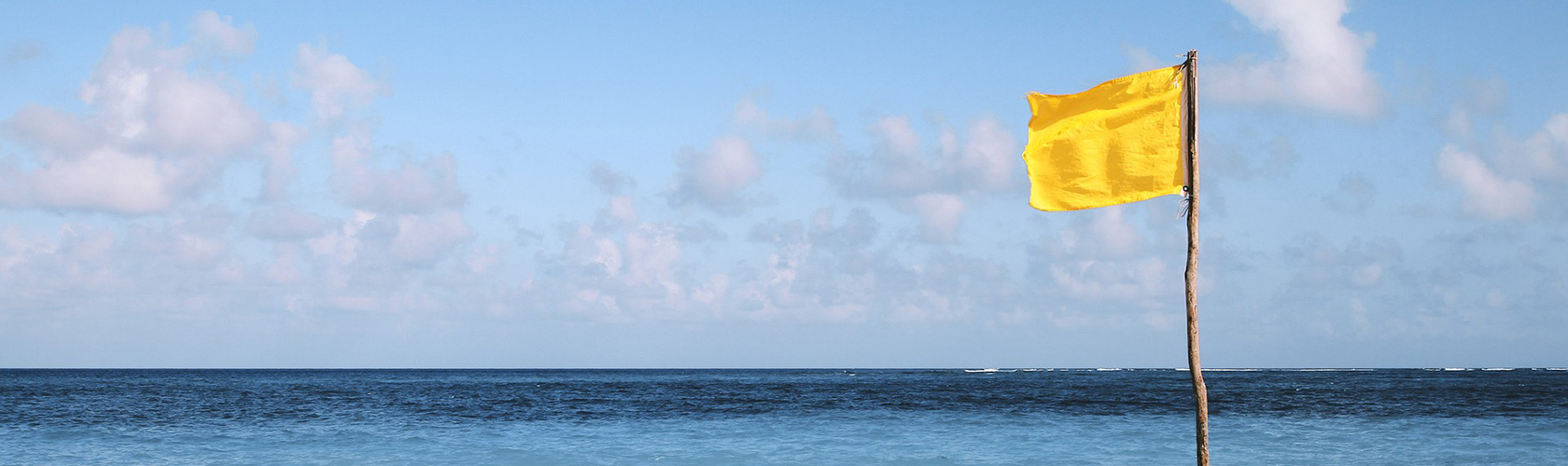 Eine gelbe Flagge weht im Wind. Im Hintergrund das Meer